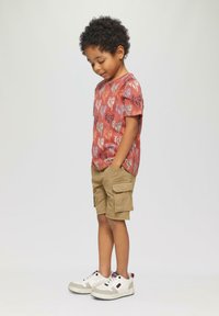 Enfant portant un t-shirt rouge à manches courtes avec un imprimé de palmier, un short cargo kaki et des baskets blanches avec des accents gris.