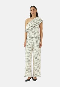 Black polka dot design on white fabric, featuring a one-shoulder top with a ruffled detail and loose, wide-legged pants.