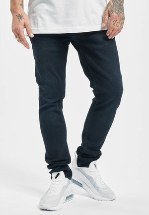 Tmavě modré slim-fit džíny, směs bavlny, s hladkou texturou a minimálním prošíváním. Spárovány se světle šedými a bílými teniskami s akcenty.