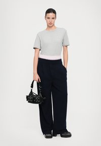 Camiseta gris de manga corta con una cinturilla a rayas en tonos rosa y blanco, combinada con pantalones de pierna ancha en color navy y un pequeño bolso negro.