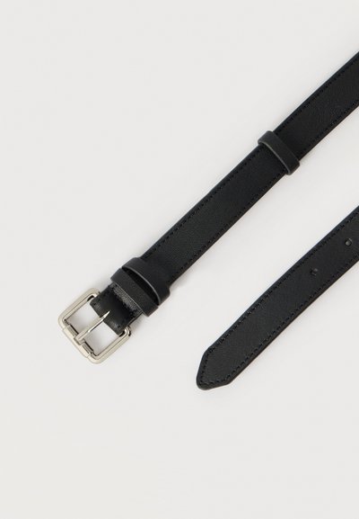 Μαύρη δερμάτινη ζώνη με ασημί μεταλλική αγκράφα. Διαθέτει ομαλή υφή και ρυθμιζόμενες τρύπες για το καμάκι. Καταλήγει σε μυτερή άκρη.