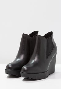 Botines de cuña de piel negra con paneles laterales elásticos, punta redonda y suela texturizada. Acabado liso con detalles mínimos.