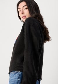 Svart ribbestrikket genser med lange ermer, rund hals og en litt kort design. Brukt over blå denimjeans.