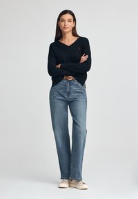 Czarny sweter w serek, luźny krój, noszony z jasnoniebieskimi spodniami straight-leg, brązowym paskiem i beżowymi trampkami. Prosty design z minimalnymi akcentami.