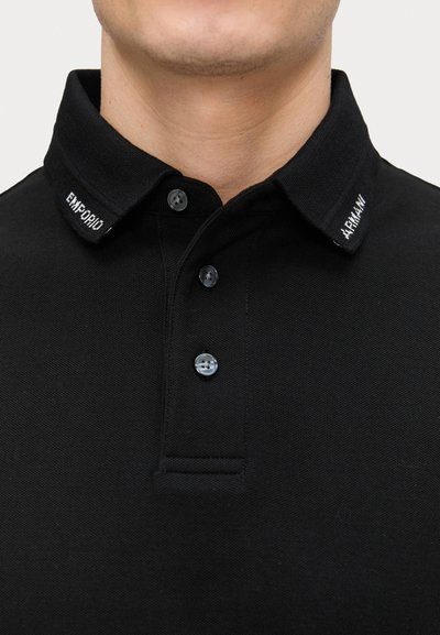 Black polo shirt with a textured fabric, featuring a classic collar, three buttons, and embroidered brand name on the collar.