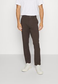 Bruna rutig byxor med skräddarsydd passform och slät textur. Matchade med en enkel vit t-shirt och ljusfärgade sneakers.