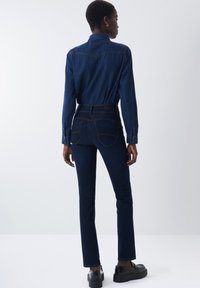 Camisa y pantalones de mezclilla oscura, con un diseño ajustado, detalles de costura sutiles y una textura suave. Unos zapatos de plataforma negros completan el look.