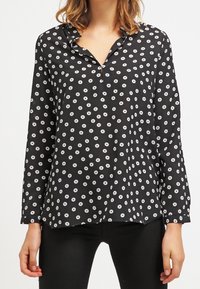 Blusa nera con colletto, caratterizzata da un motivo a pois bianchi circolari, maniche lunghe e una vestibilità ampia. Tessuto dalla texture liscia.