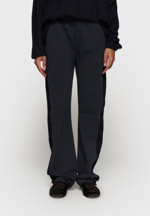 Pantaloni da tuta a gamba larga blu navy con vita elastica, cordoncino regolabile, tasche laterali e pannelli laterali neri a contrasto.