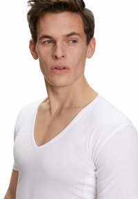 T-shirt bianco in cotone con scollatura a V profonda e maniche corte. Il tessuto appare liscio e leggero, con un design semplice e pulito.