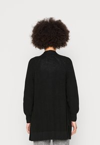 Černý dlouhý kardigan s texturovaným pleteným vzorem, žebrovanými manžetami a lemem a bočními rozparky pro větší pohyblivost. Otevřený zadní díl s jemným designovým detailem.