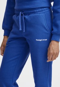 Blå bomuldsjoggingbukser med elastisk talje og snoretræk. Har et lille hvidt logo på venstre lår. Glat tekstur, afslappet design.