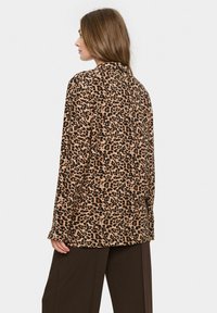 Blazer s leopardím vzorom v odtieňoch hnedej a čiernej, mäkký materiál, uvoľnený strih, dlhé rukávy, záklapkový golier a bočné rozparky.