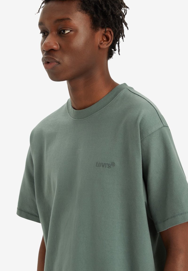 Grünes Baumwoll-T-Shirt mit Rundhalsausschnitt und kurzen Ärmeln. Mit einem dezenten grauen Levi's-Logo auf der Brust. Glatte Textur und lockere Passform.