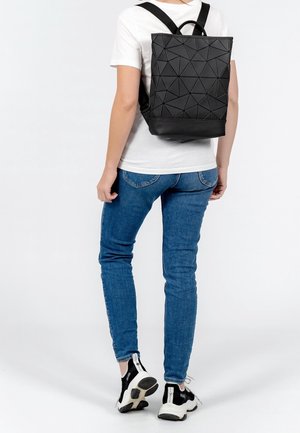 Zaino nero con motivo geometrico realizzato in materiale sintetico, dotato di spallacci regolabili e maniglia superiore, posizionato sulla schiena di una persona.