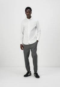 Lightweight white long-sleeve shirt with a button-down collar, paired with gray tapered pants and black sneakers with white accents.