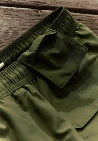 Olívazöld, rugalmas derékú rövidnadrág texturált folttal és oldalzsebbe, sima anyaggal és letisztult szabással.