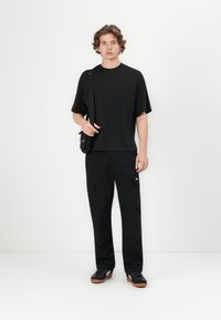 Sort crew-neck t-shirt med korte ærmer, parret med sorte cargo-bukser med flere lommer. Sorte sko med brune såler.