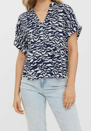 Vrouw draagt een marineblauw-wit patroon kort mouw blouse met V-hals, gecombineerd met lichtblauwe jeans met hoge taille.
