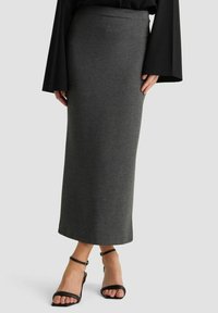 Grauer, taillierter Maxirock aus weichem Stoff. Hat eine hohe Taille und reicht bis zu den Knöcheln, kombiniert mit schwarzen Riemchensandalen.