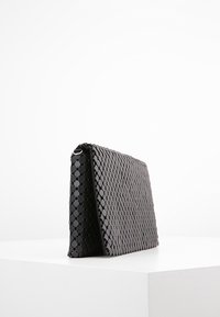 Borsa a tracolla nera intrecciata con motivo esagonale, design piatto, texture liscia e un profilo laterale distintivo. Presenta un dettaglio in hardware argentato.
