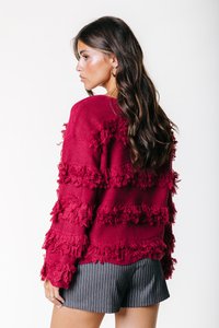 Pull bourgogne avec des détails de frange texturés, design en tricot, coupe décontractée et manches longues, associé à un short à rayures.