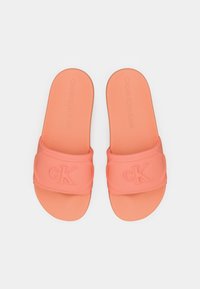 Paire de sandales slides rose corail avec logo embossé "cK" sur les brides et texte "Calvin Klein Jeans" sur les semelles, sur fond blanc.