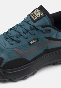 Adidașii Vans în nuanțe de albastru și negru au un superior din țesătură texturată, cu accente netede, șireturi rotunde și o talpă groasă din cauciuc negru.