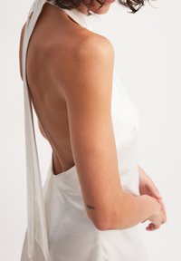 Vestido de satén blanco con cuello halter y espalda descubierta, que cuenta con una textura suave y una tela drapeada que cae por los hombros.