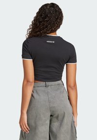 Černé zkrácené tričko s přiléhavým střihem, krátkými rukávy s bílým lemem a vyšitým logem Adidas na zadním výstřihu.