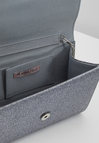 Silver glittrande clutch med grått innertyg, som har ett kortfack, kedjetillbehör och tryckknappslås. Slät yta genom hela väskan.