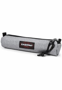 Estuche de lápices de tela gris con forma cilíndrica, cremallera negra y parche con el logo de Eastpak, con un acabado texturizado y un lazo para colgar.