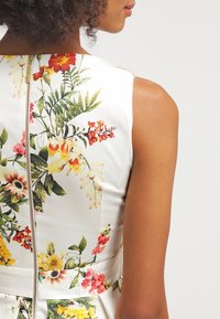 Vestido de tela blanca con estampado floral de flores vibrantes, que cuenta con un cierre en la parte trasera y un diseño ajustado. Mangas cortas y textura suave.