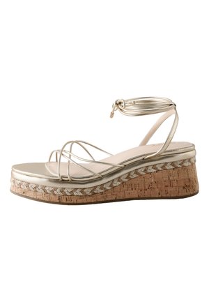 Sandale à plateforme beige avec semelle en liège, plusieurs fines lanières sur les orteils et sangle autour de la cheville nouée en nœud.
