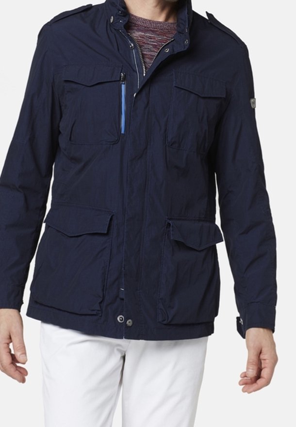 Veste coupe-vent bleu marine avec quatre poches, fermeture éclair et un design structuré. Dotée d'un col montant et d'un tissu léger.