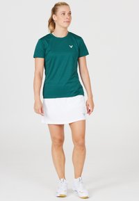 Kortærmet, grøn sports shirt parret med en hvid nederdel. Bemærkelsesværdig logo på skjorten og en glat stofstruktur. Hvide athletic sko.