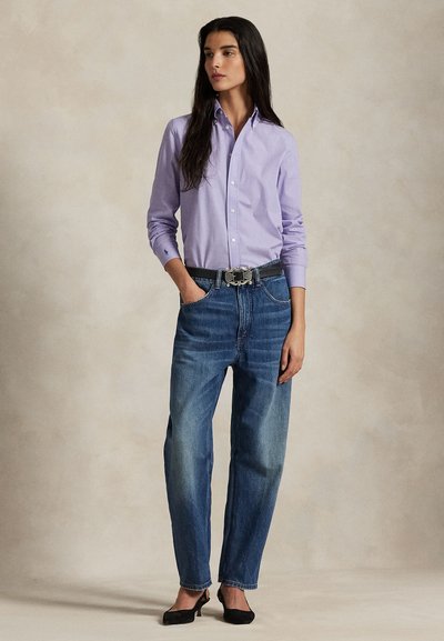 Heleroosa nööpidega särk, sinised teksapüksid kõrge vöökohaga, must vöö hõbedase pandlaga, mustad kontsakingad, tekstuuriga taust.