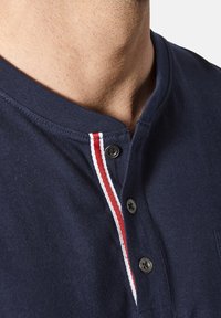 Navy blue cotton polo shirt with a henley neck, featuring two buttons and white and red striped accents along the collar.