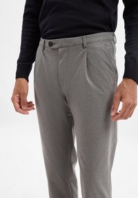 Gray tailored trousers with a subtle texture, single pleats, belt loops, and a button closure, worn with a black sweater.