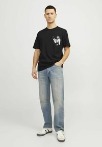 Sort kortærmet t-shirt med en lomme, der har et hvidt grafisk motiv, kombineret med lyseblå lige ben jeans og hvide sneakers.