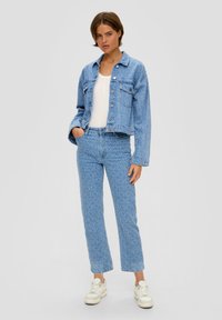 Veste en denim bleu clair avec un col et des poches avant, associée à un jean bleu clair à motifs. Comprend des baskets blanches.