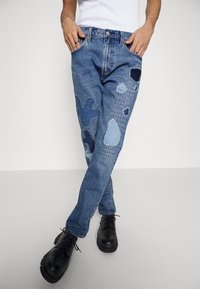 Jeans i ljusblå denim med olika patchade mönster i mörkblått och ljusblått med broderade detaljer. Standard femfickorsdesign.