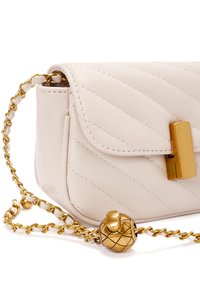Beige, gebogen leren tas met een gouden kettinghengsel. Heeft een gouden sluiting en een decoratieve ananasvormige hanger aan de ketting.