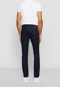 Granatowe dżinsy o dopasowanym kroju, pięciopocketowym designie i skórzanej metce z tyłu. W zestawieniu z białą koszulką i białymi butami.