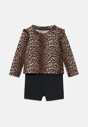 Bluzka z długim rękawem w panterkę z falbankami, zestawiona z czarnymi szortami. Miękka tkanina o gładkiej fakturze. Posiada okrągły dekolt.