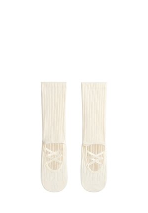 Paire de chaussettes côtelées couleur crème avec des brides élastiques croisées style ballet à l’ouverture du pied, étalées à plat sur un fond blanc.