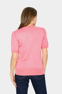 Rosa kurzärmeliger Pullover mit geripptem Kragen und Saum, glatte Textur, körperbetontes Design, kombiniert mit dunkelblauen Jeans.