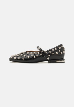 Black leather flats with rounded toe, embellished with silver studs across the upper and a buckle strap. Flat heel with metallic accent.