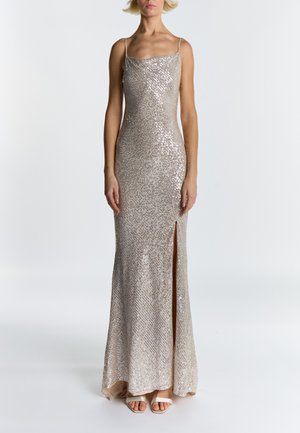 Pitkä, vartalonmyötäinen iltapuku metallinhohtoisessa beigen sävyisessä kankaassa, jossa on paljetteja, ohuet olkaimet ja reiden korkuinen sivuhalkio. Sileä pinta ja kiilto.