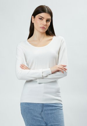 Suéter blanco de manga larga con escote de barco y puños y dobladillo acanalados. Combinado con jeans azules, mostrando una textura suave y lisa.